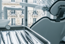 Close-up of sterile dental instruments on a tray in a modern, clean dental clinic. In the soft-focus background, through a window, classic French architecture is visible under bright, natural light.
