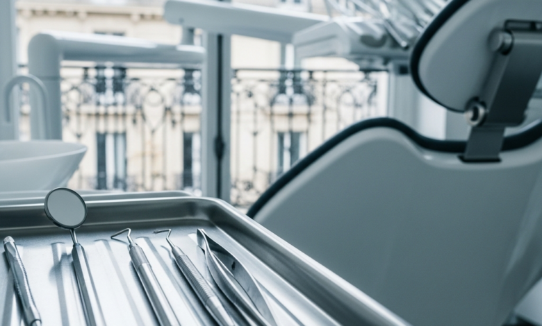 Close-up of sterile dental instruments on a tray in a modern, clean dental clinic. In the soft-focus background, through a window, classic French architecture is visible under bright, natural light.