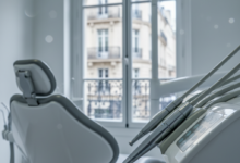 A sharp, detailed close-up of modern dental equipment, possibly a polished dental instrument or part of a dental chair, within a bright, clean, and contemporary dental treatment room. In the soft-focus background, a blurred window reveals a hint of classic French architecture, such as a traditional Parisian building facade, under subtle, professional lighting. The scene suggests advanced healthcare and a structured environment, with no visible text or branding.