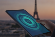 Close-up of a hand holding a digital tablet displaying abstract, overlapping layers of financial coverage in blues and greens. In the blurred background, the iconic silhouette of the Eiffel Tower rises above Parisian rooftops under a soft sky, signifying France's healthcare system.