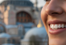 Un sourire radieux et confiant, aux dents parfaitement blanches et alignées, est le point focal. L'arrière-plan est un paysage urbain fortement flouté montrant la silhouette d'un monument historique d'Istanbul, comme la Mosquée Bleue ou Sainte-Sophie, baigné de lumière naturelle douce.